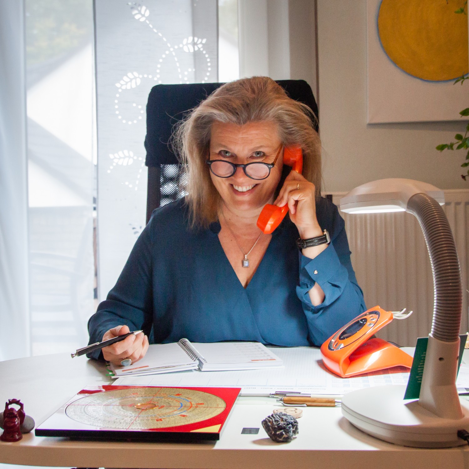 lächelnde Feng Shui Beraterin Bischoff in ihrem Büro mit ihrem orangen Telefonhörer am Ohr im Kreis Stormarn